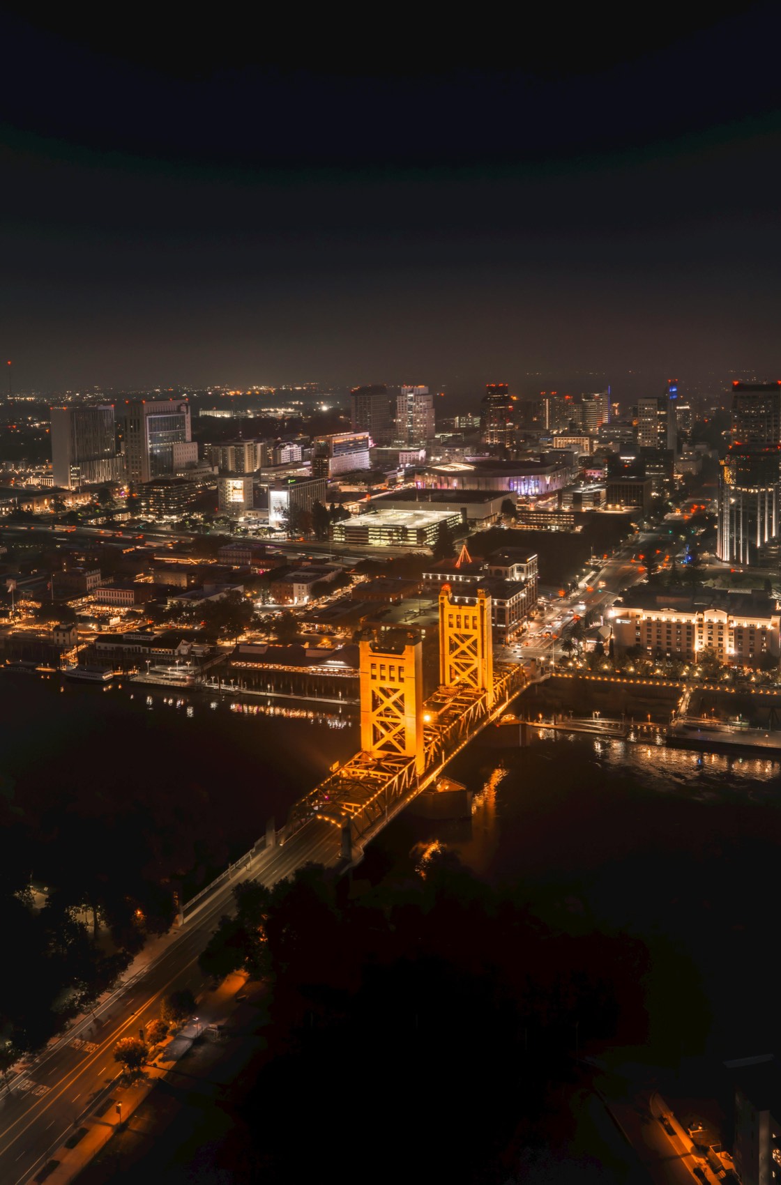 Sacramento's Tower Bridge lit up gold at night above the river.
